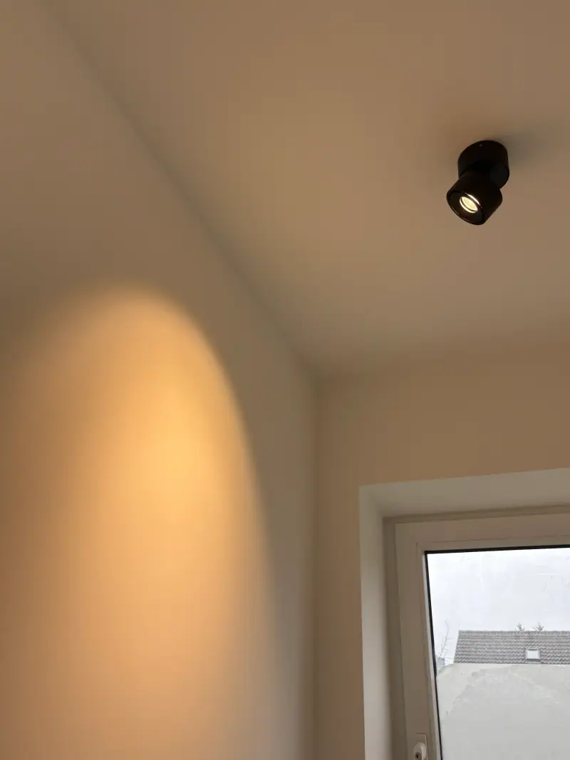 Deckenspot, der warmes Licht an eine helle Wand wirft