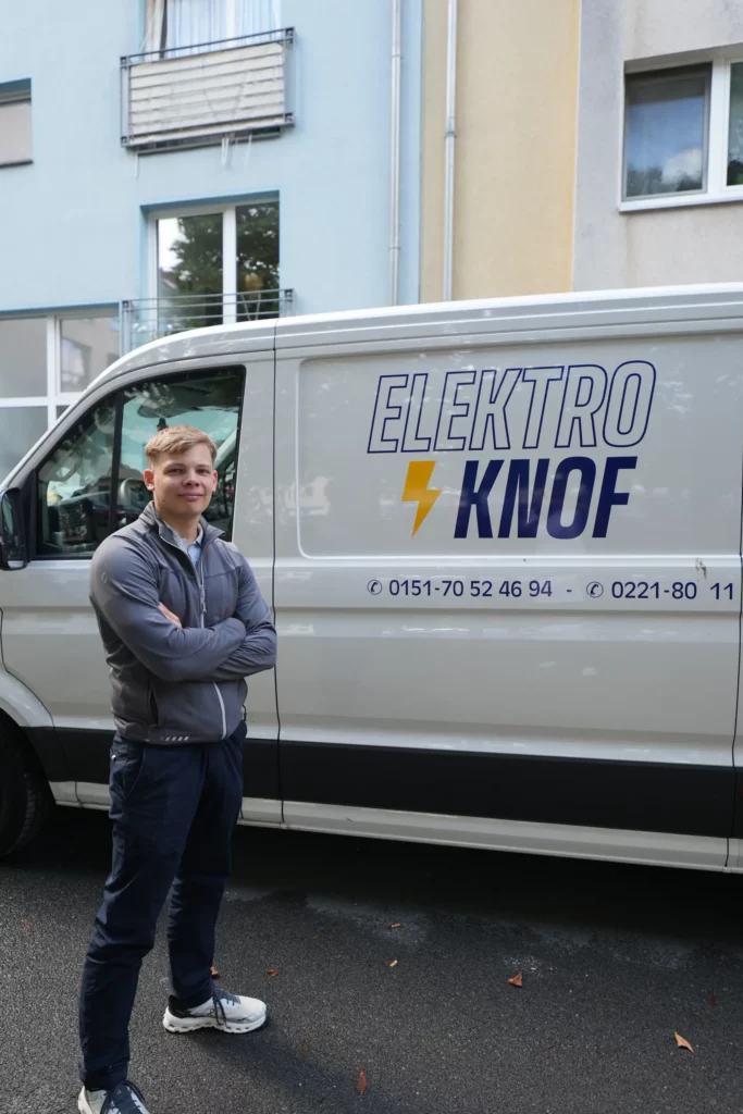 Techniker steht vor weißem Firmenfahrzeug mit Elektro Knof Logo und Blitzzeichen