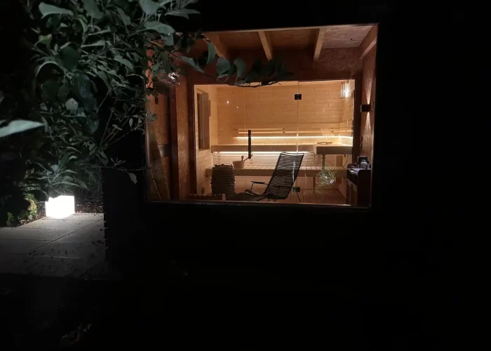 Moderner Saunaraum mit Holzverkleidung, Bank und Liege, beleuchtet durch große Glasfront bei Nacht